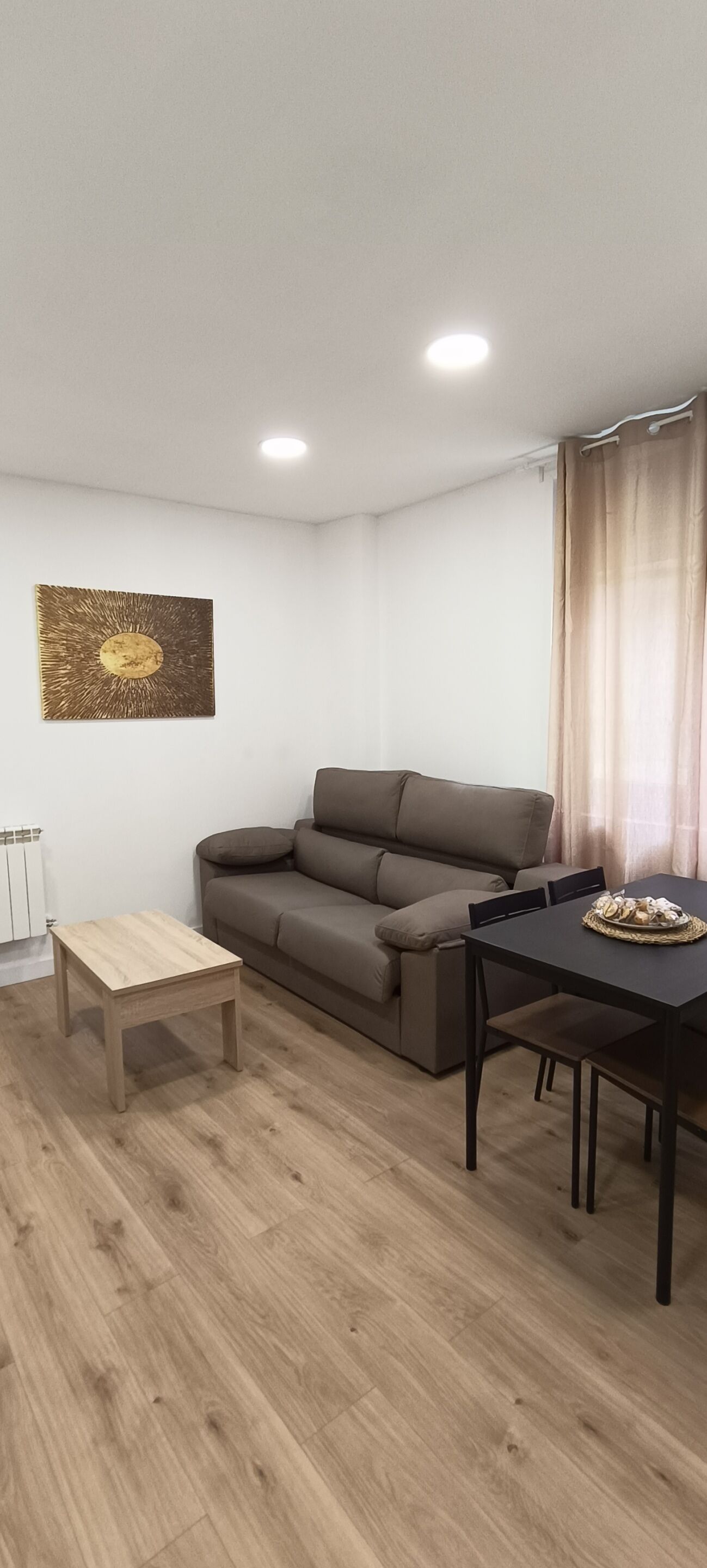 A modern living room with a brown sofa, a wooden coffee table, and a dining table with chairs.