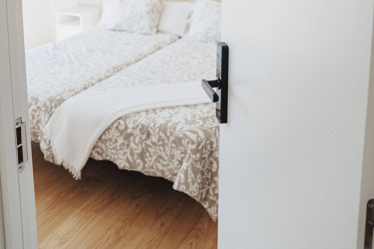 A bedroom with a bed, a bedside table, a hanging light fixture, and a door with the number 202.