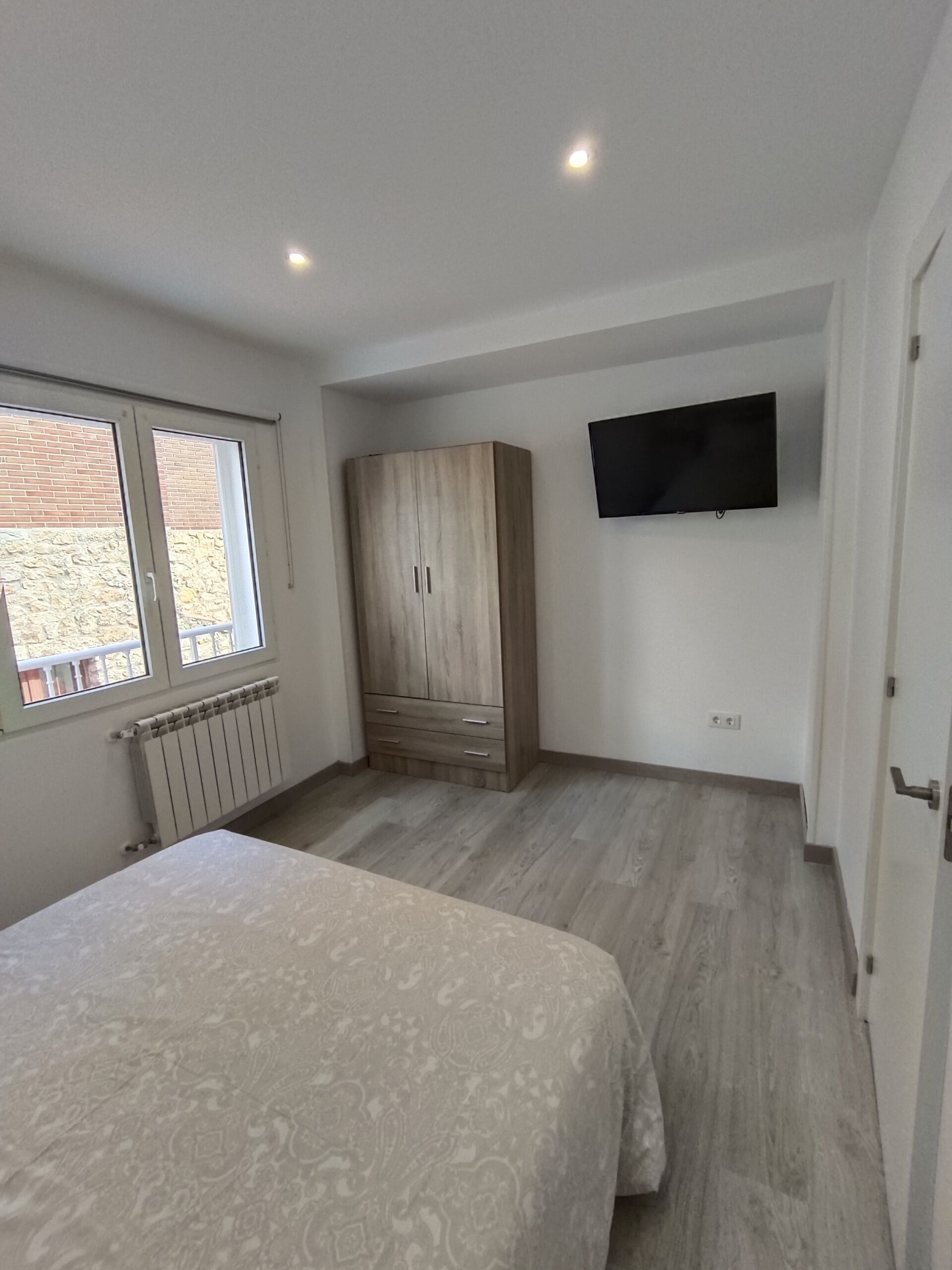 Un dormitorio con cama, armario, televisión y ventana.