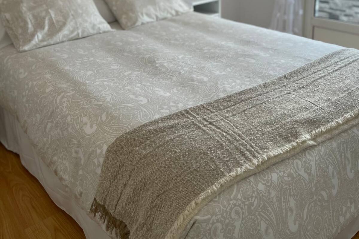 A neatly made bed with a patterned bedspread and a textured throw blanket.