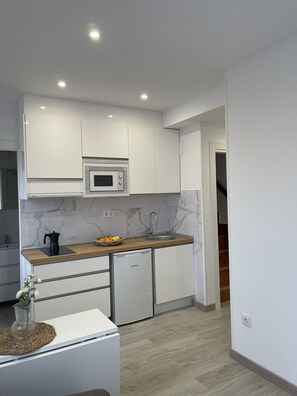 A modern kitchen with white cabinetry, a built-in microwave, and a wooden countertop. - Hotel Posada del Mar (Suances)