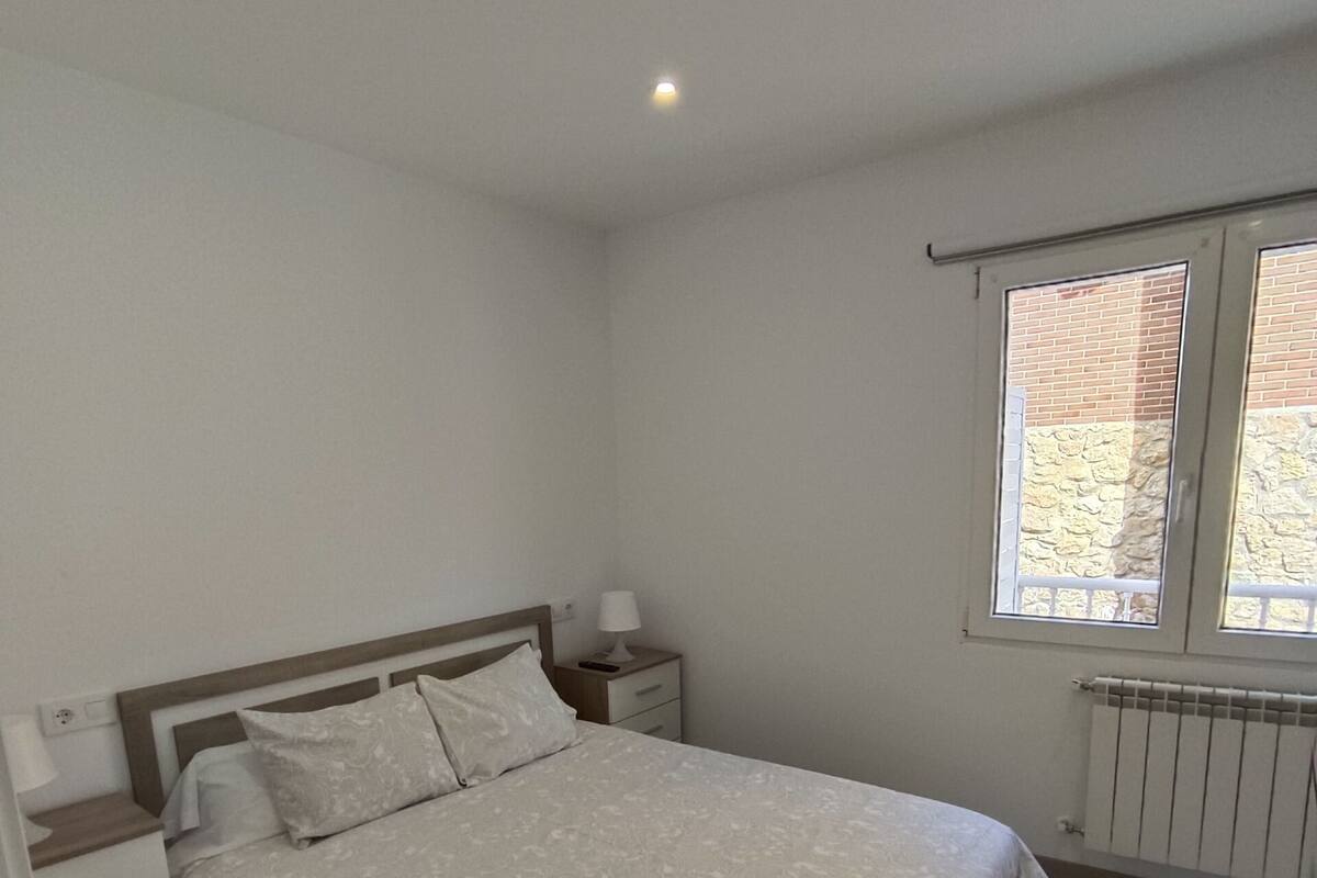 A bedroom with a bed, bedside tables, a window with a view, and a radiator.