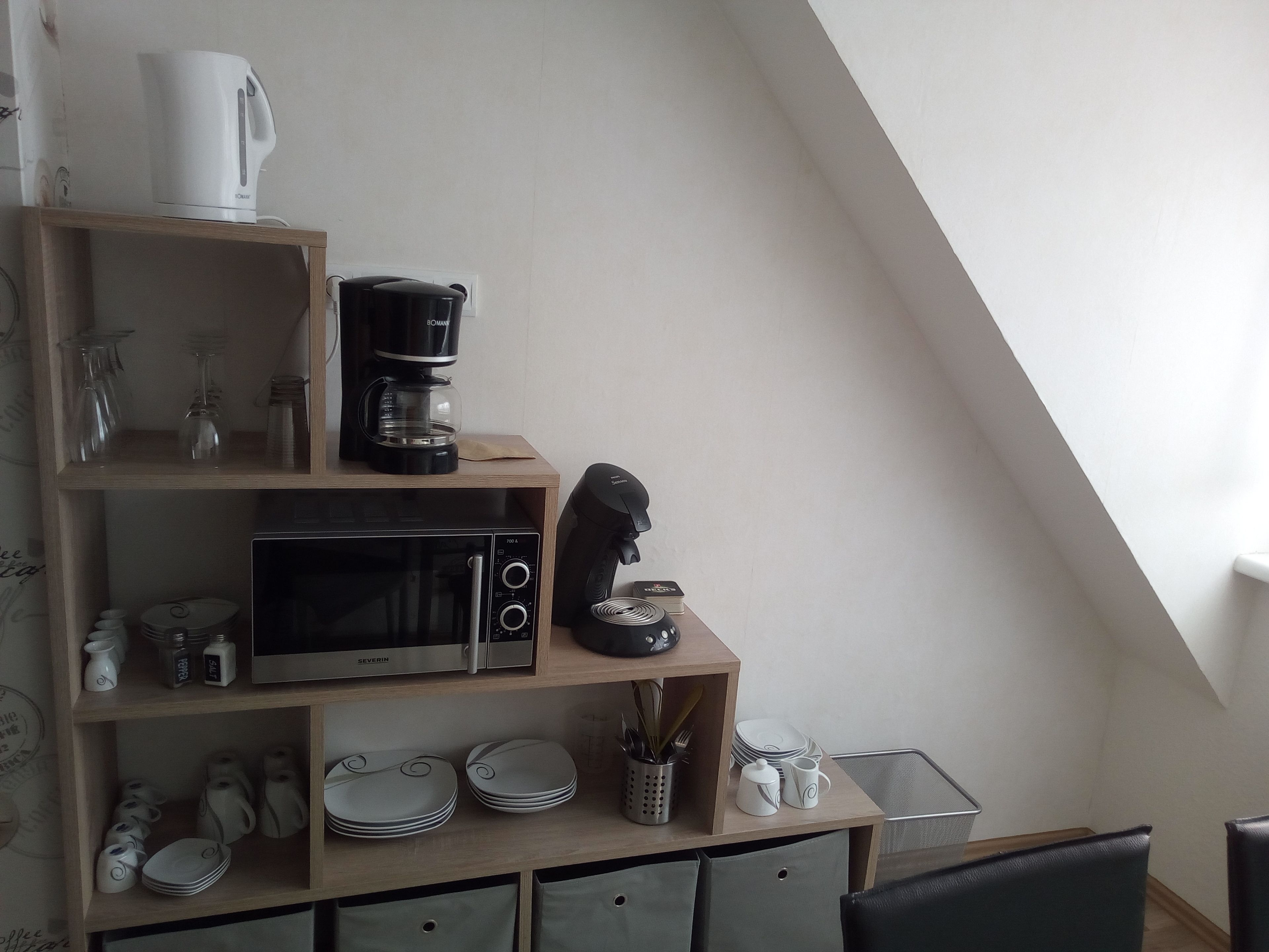Ett kök med mikrovågsugn, kaffebryggare och hyllor med tallrikar och köksredskap.