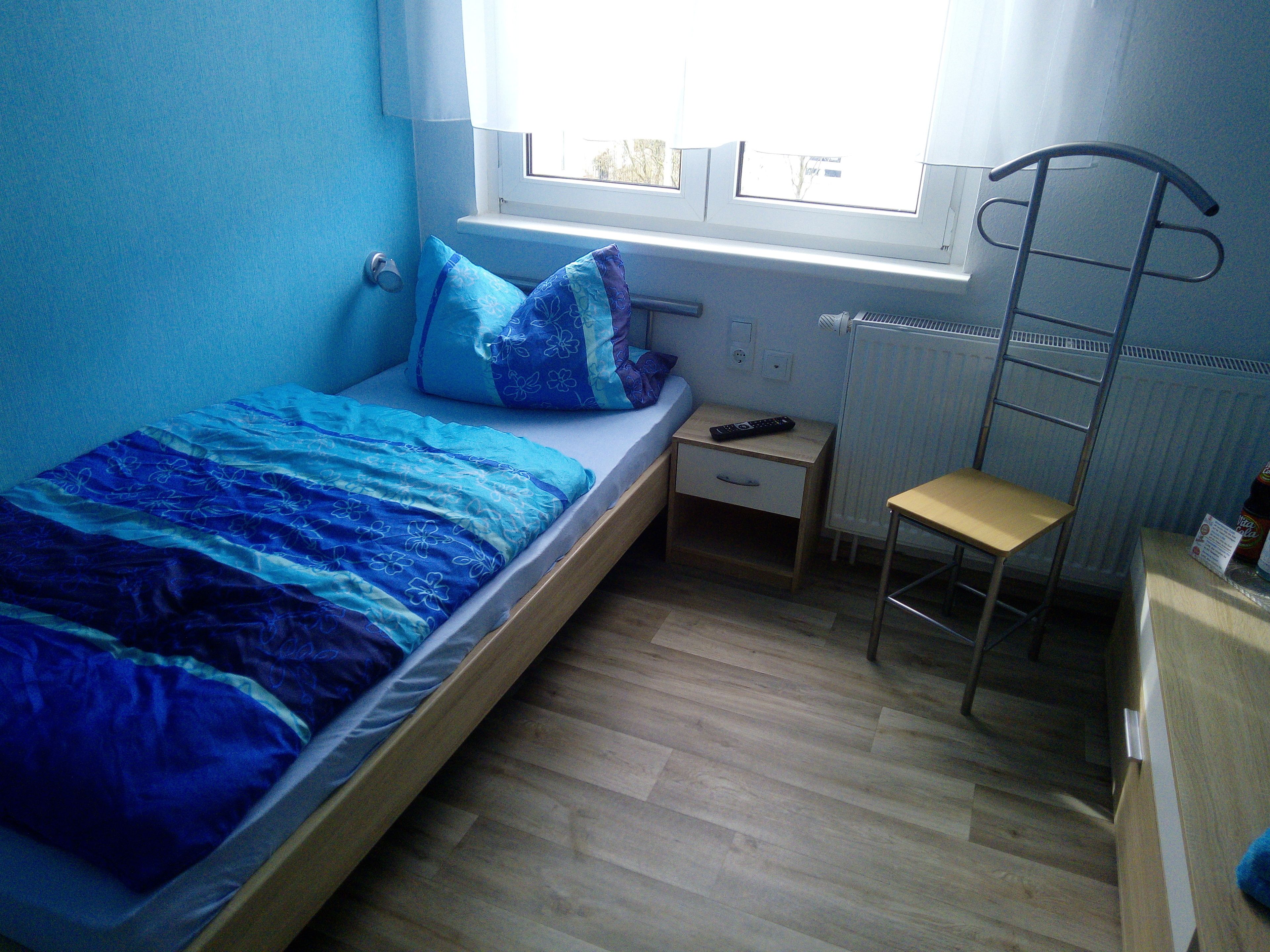 A bedroom with a single bed, a nightstand, a chair, a radiator, and a window.
