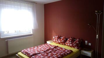 Ein Schlafzimmer mit Bett, Nachttisch, Stehlampe und einem Fenster mit Vorhängen.