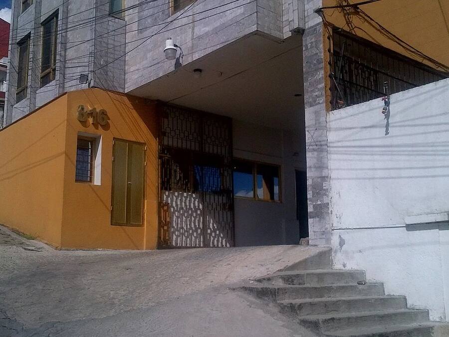 Un edificio con fachada amarilla, entrada protegida por una reja y una escalera que lleva a una puerta.