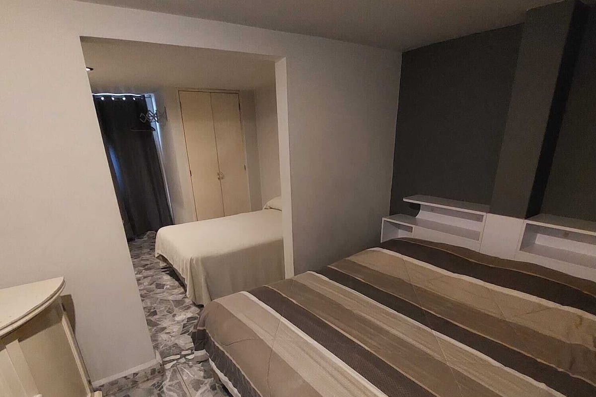 A bedroom with a bed, a small bedside table, a wardrobe, and a TV stand.