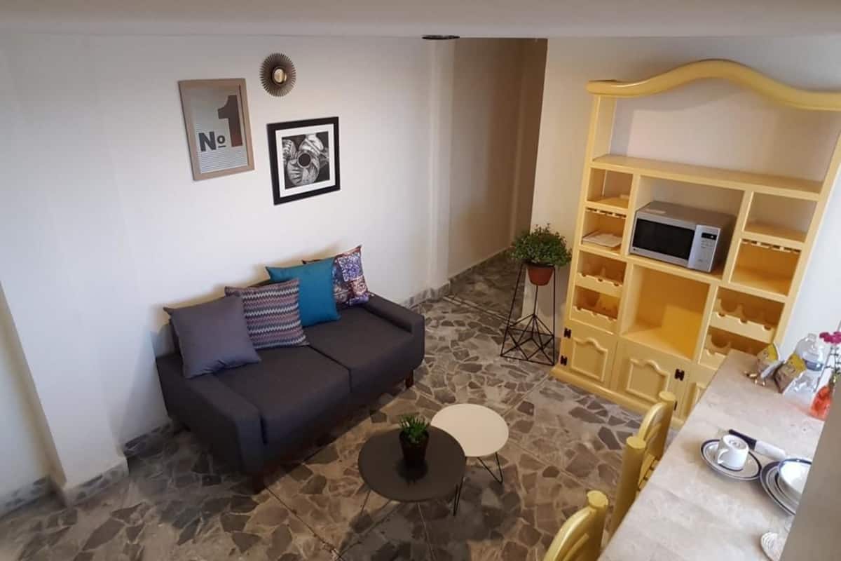 A living room with a sofa, a coffee table, a bookshelf, and a microwave.