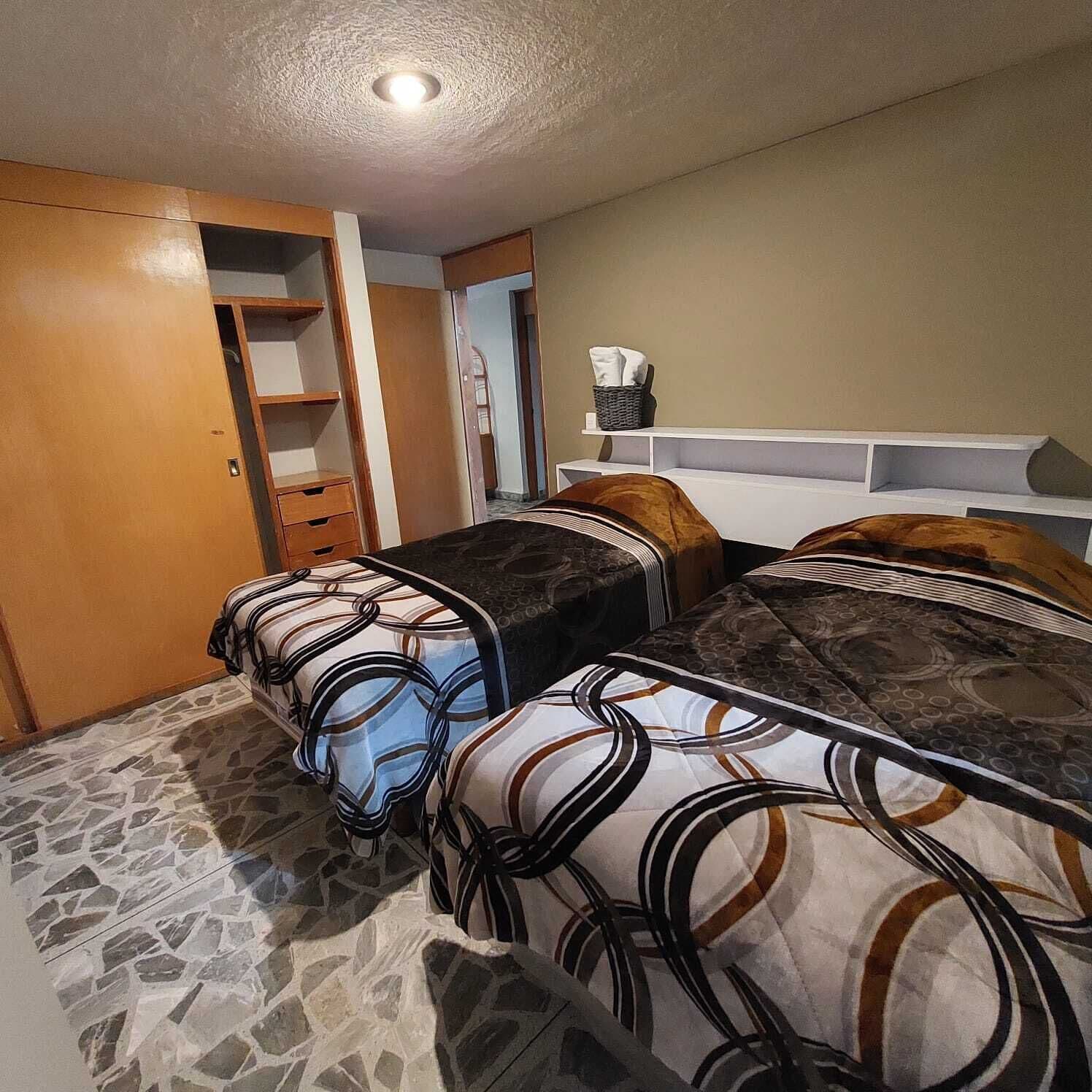 Un dormitorio con dos camas, un armario, una mesita y una estantería con una cesta.