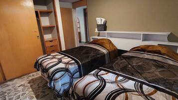Un dormitorio con dos camas, un armario, una mesita y una estantería con una cesta.