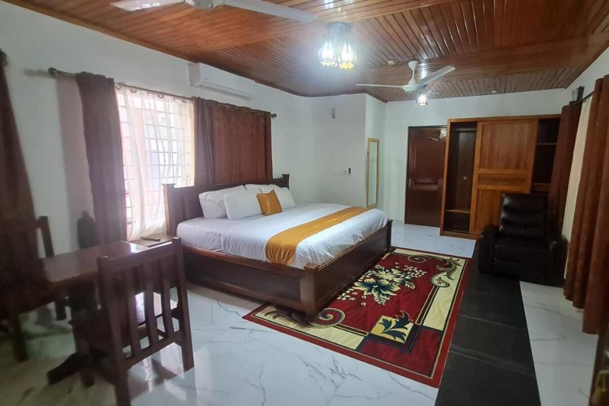 A bedroom with a bed, a desk, a chair, a ceiling fan, and a door.