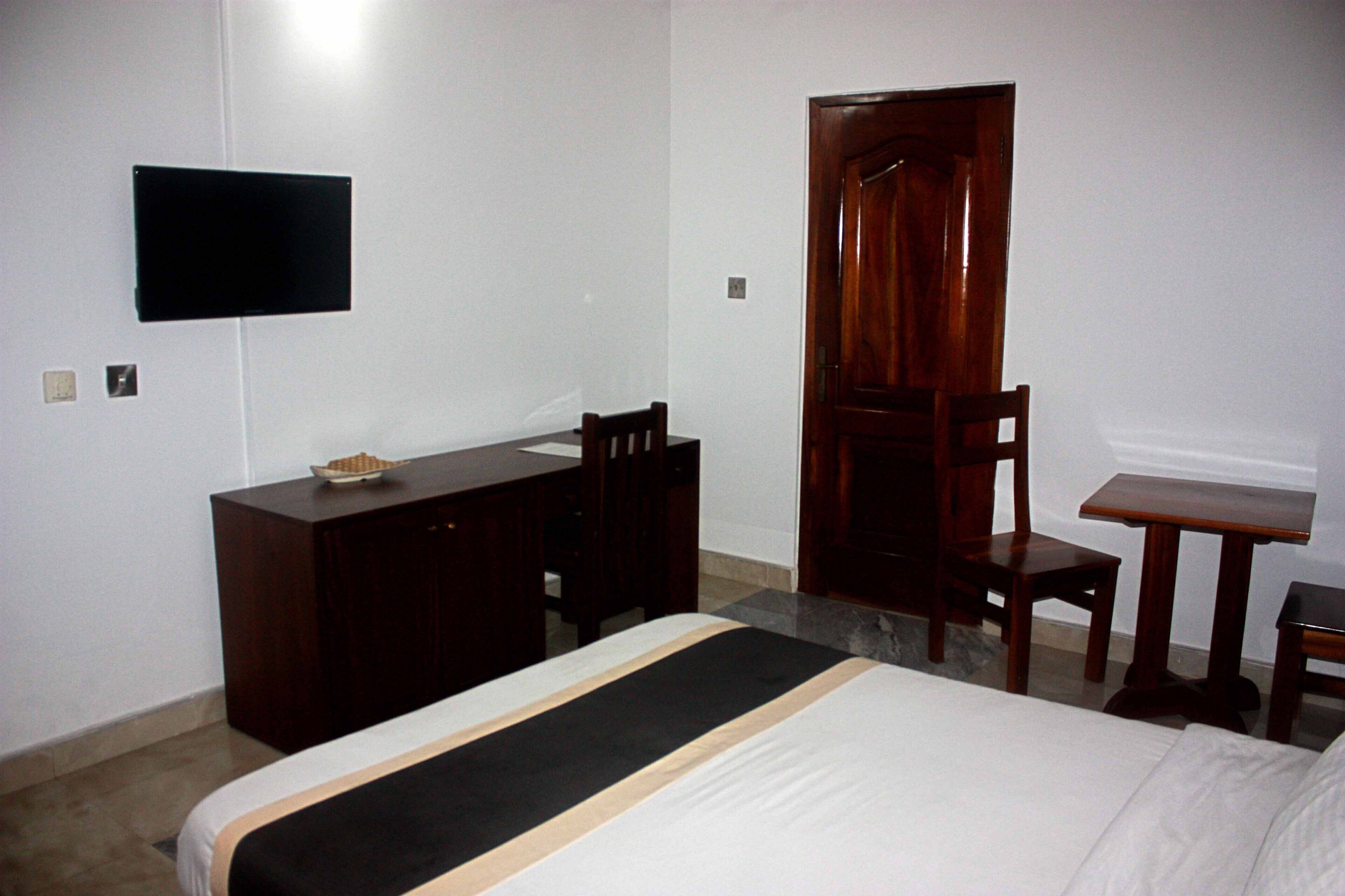 A hotel room with a bed, a wooden desk, a chair, a television mounted on the wall, and a door.