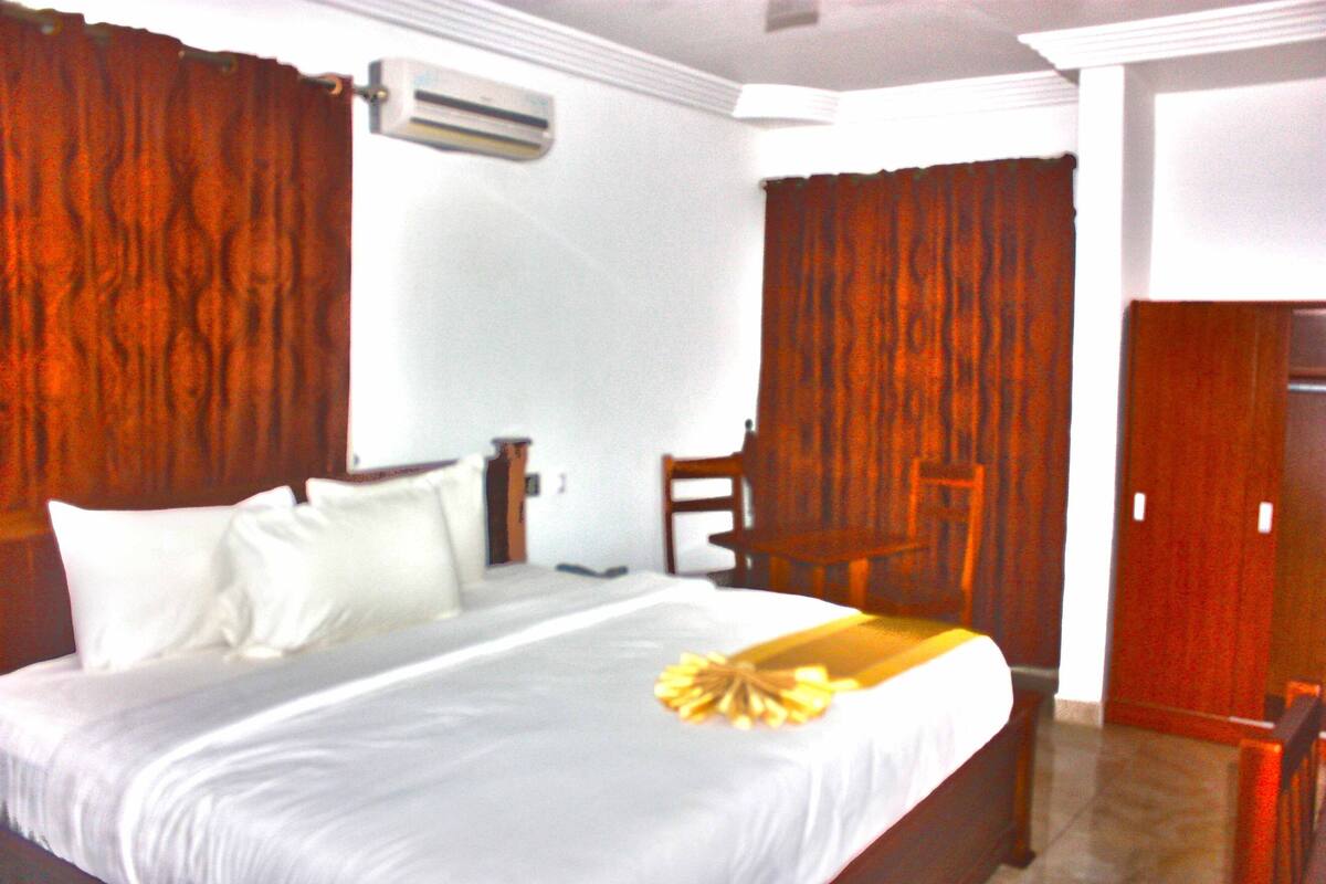 A hotel room with a bed, a chair, a desk, and a door.