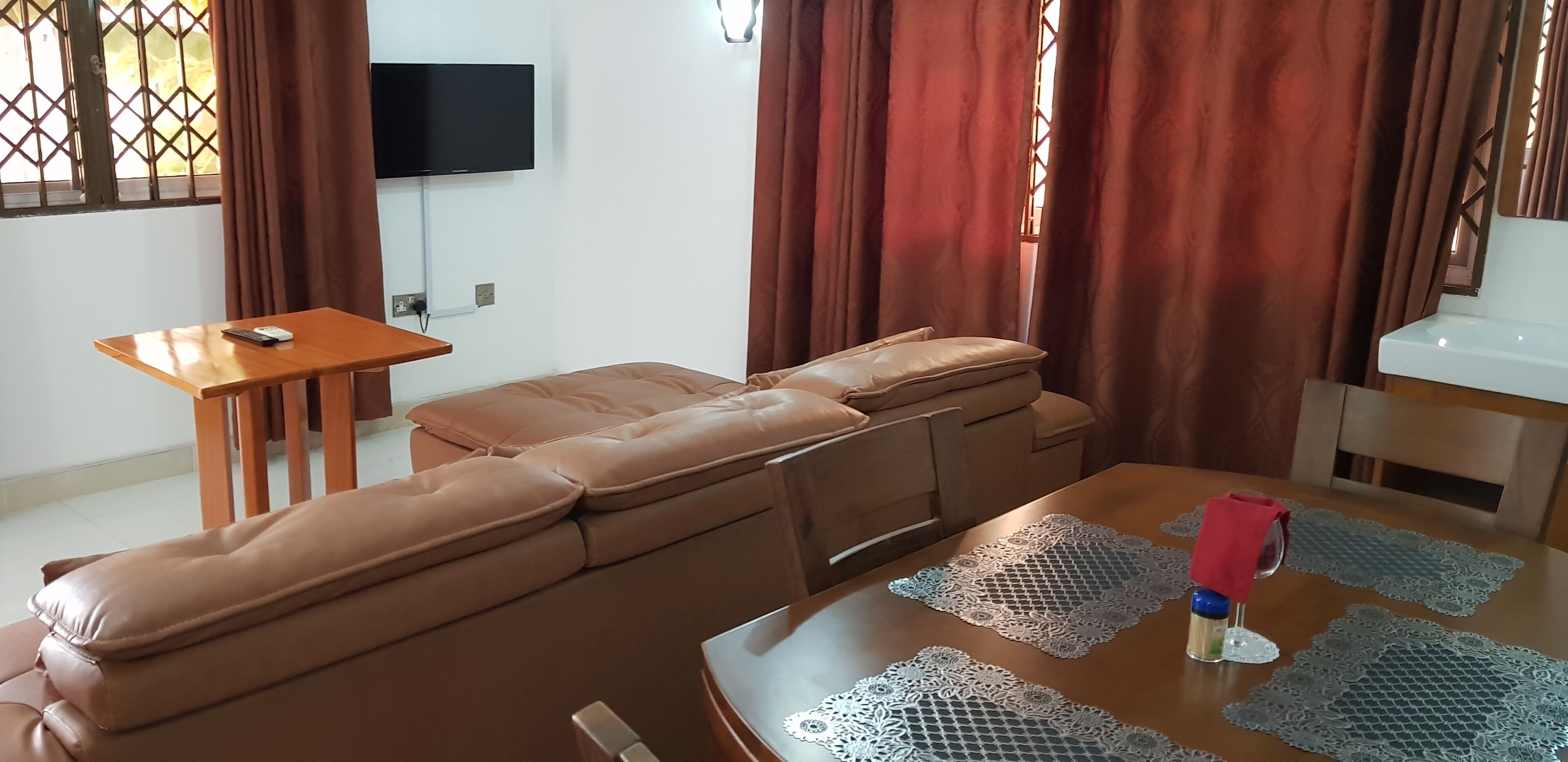 Ein Wohnzimmer mit einem braunen Sofa, einem Holztisch und einem an der Wand befestigten Fernseher.