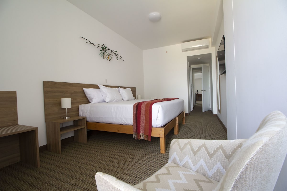 A hotel room with a bed, bedside table, lamp, and a chair.