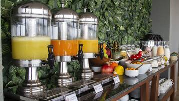 Un bufé con varios dispensadores de jugo, diversas frutas y una selección de tazones y vasos.