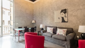 A modern living room with a grey sofa, red armchairs, a dining table with chairs, and a large window. - RSH Ara Pacis Enchanting Apartment (Rome)