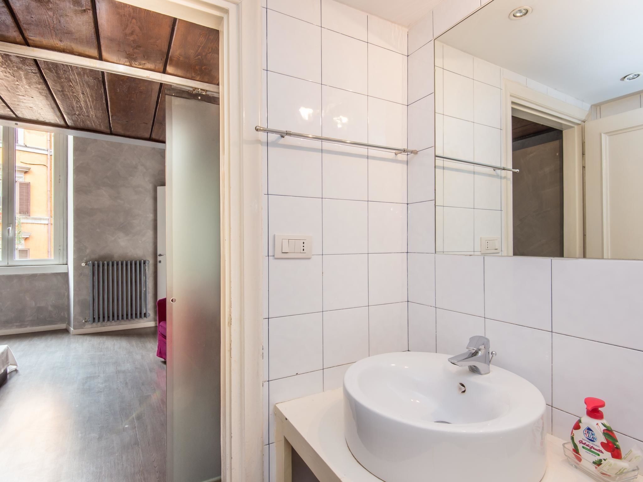 Un bagno moderno con piastrelle bianche, un lavabo rotondo, uno specchio e un termosifone.