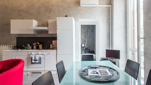 A modern kitchen with white cabinets, a red chair, and a dining table with a glass top. - RSH Ara Pacis Enchanting Apartment (Rome)