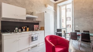 A modern kitchen with white cabinets, a red chair, and a dining area with a table and chairs. - RSH Ara Pacis Enchanting Apartment (Rome)