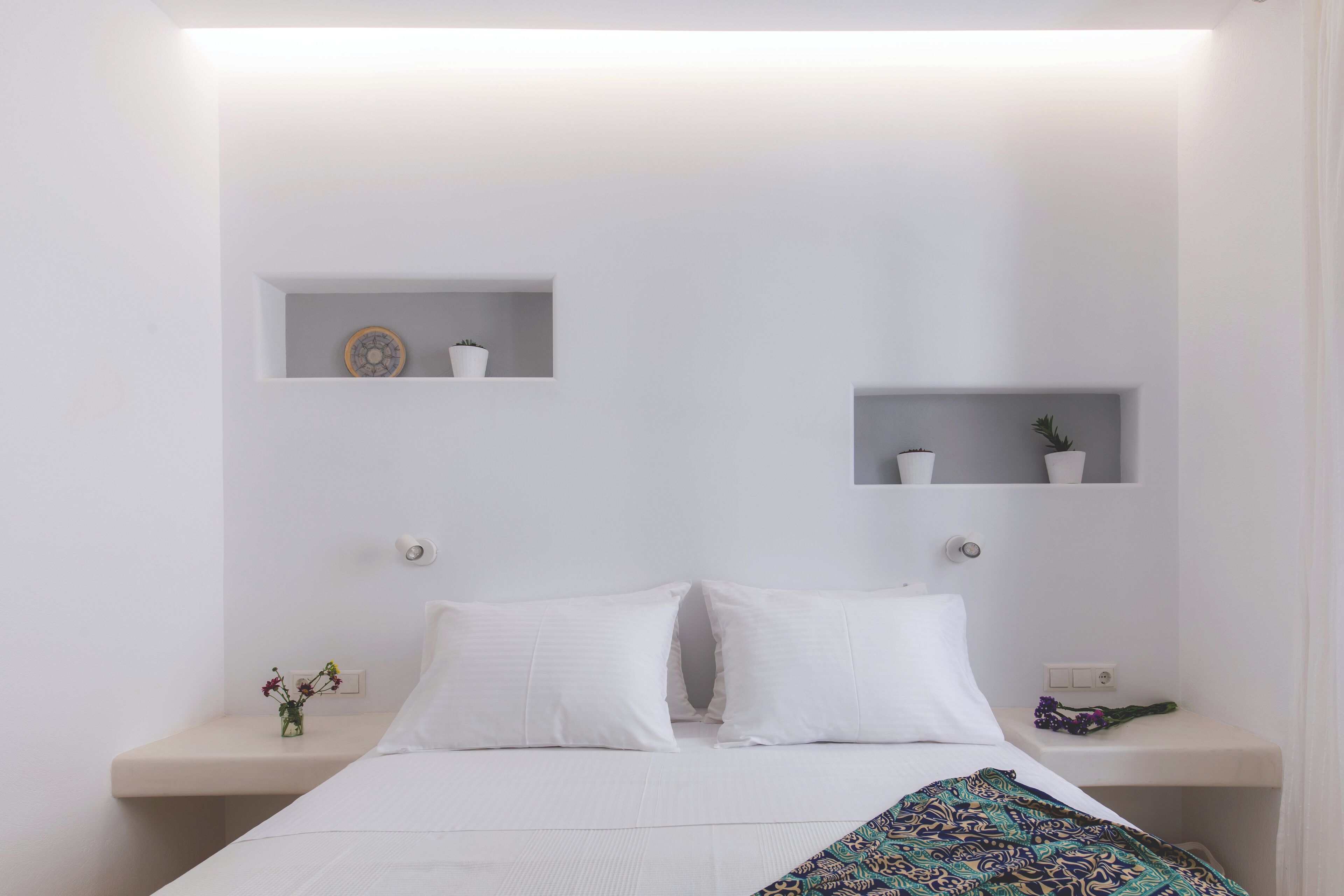 A minimalist bedroom with a bed, two bedside tables, and two wall-mounted shelves.