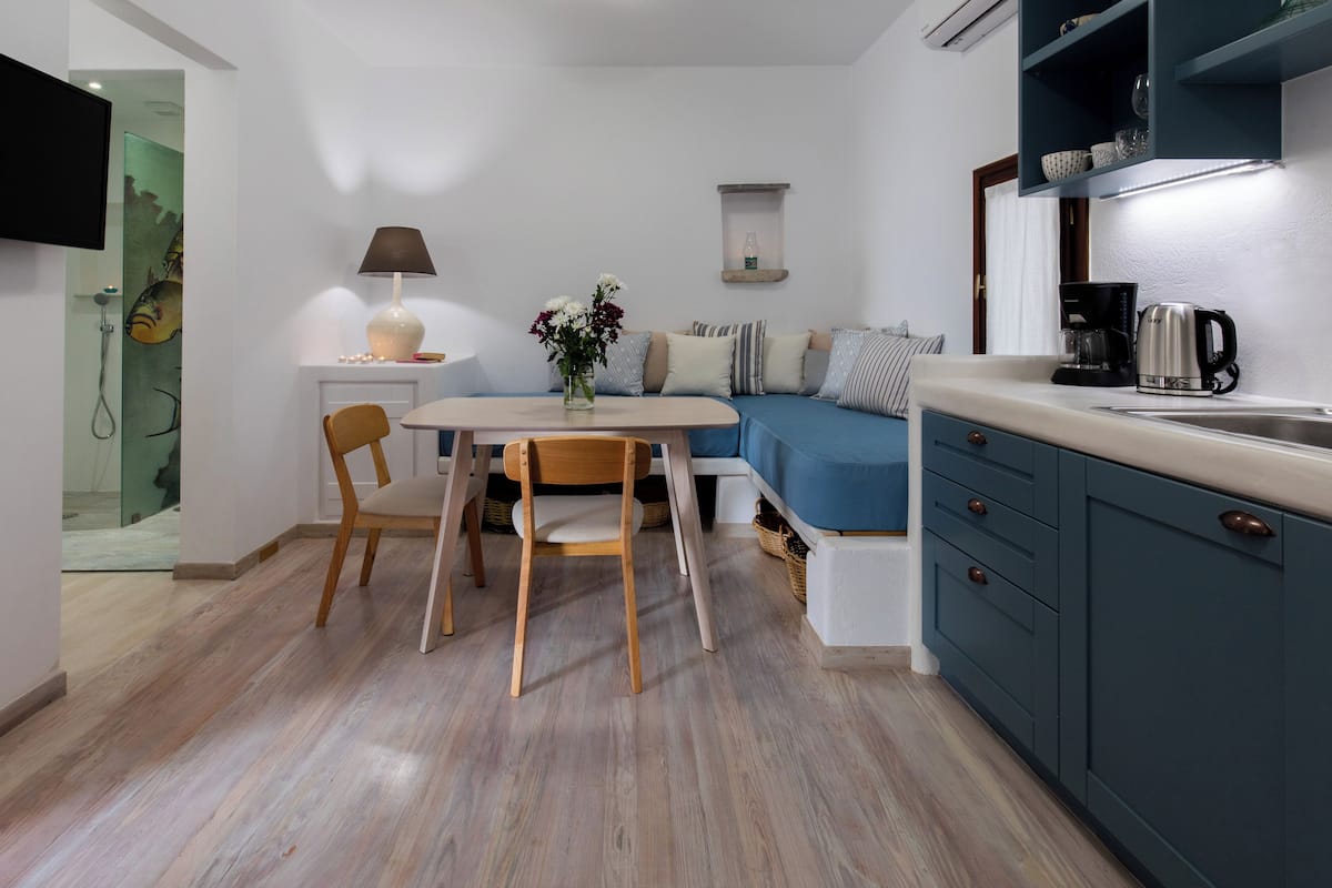 A modern kitchen with a dining area, featuring a coffee maker, a table with chairs, and a sofa with cushions.