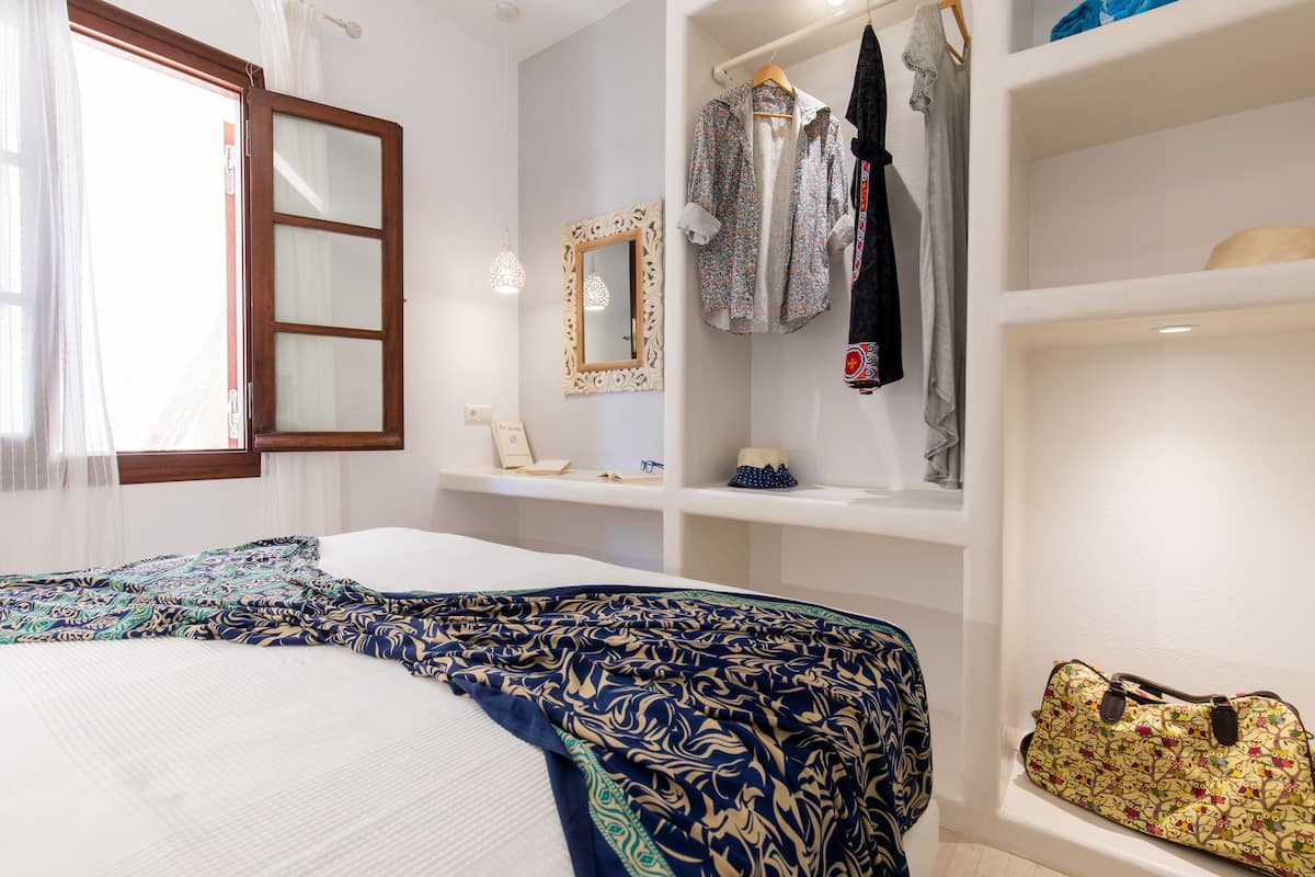 A bedroom with a bed, a wardrobe, a mirror, and a shelf with a handbag.