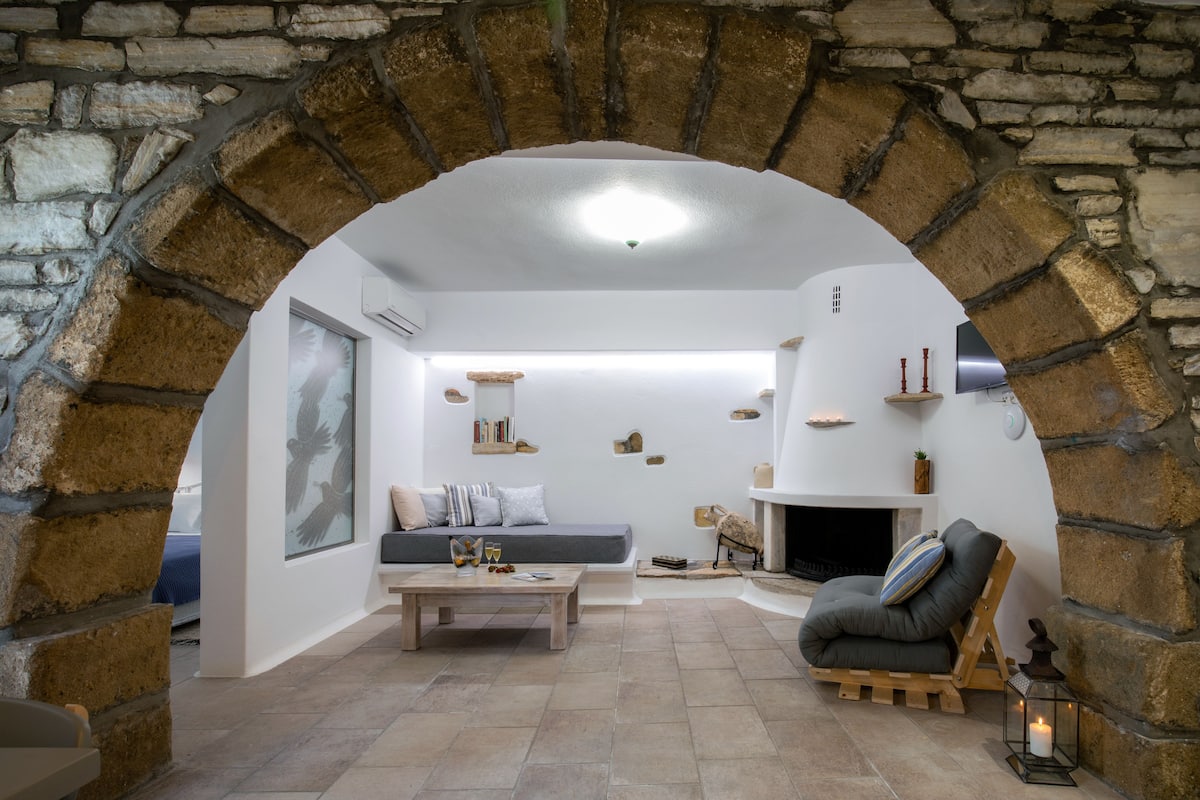 A cozy living room with a stone archway, a fireplace, a sofa, a coffee table, and a reading chair.