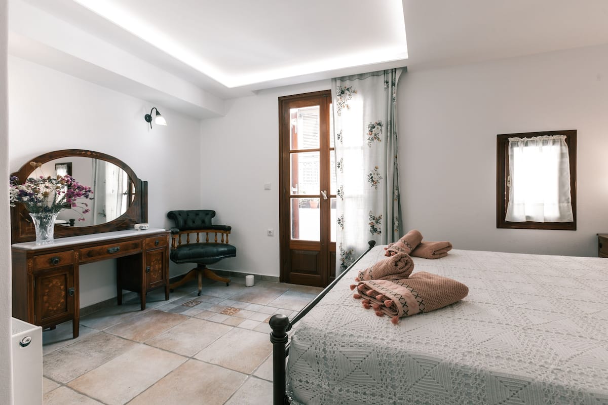 A bedroom with a bed, a dresser, a mirror, a chair, and a door.