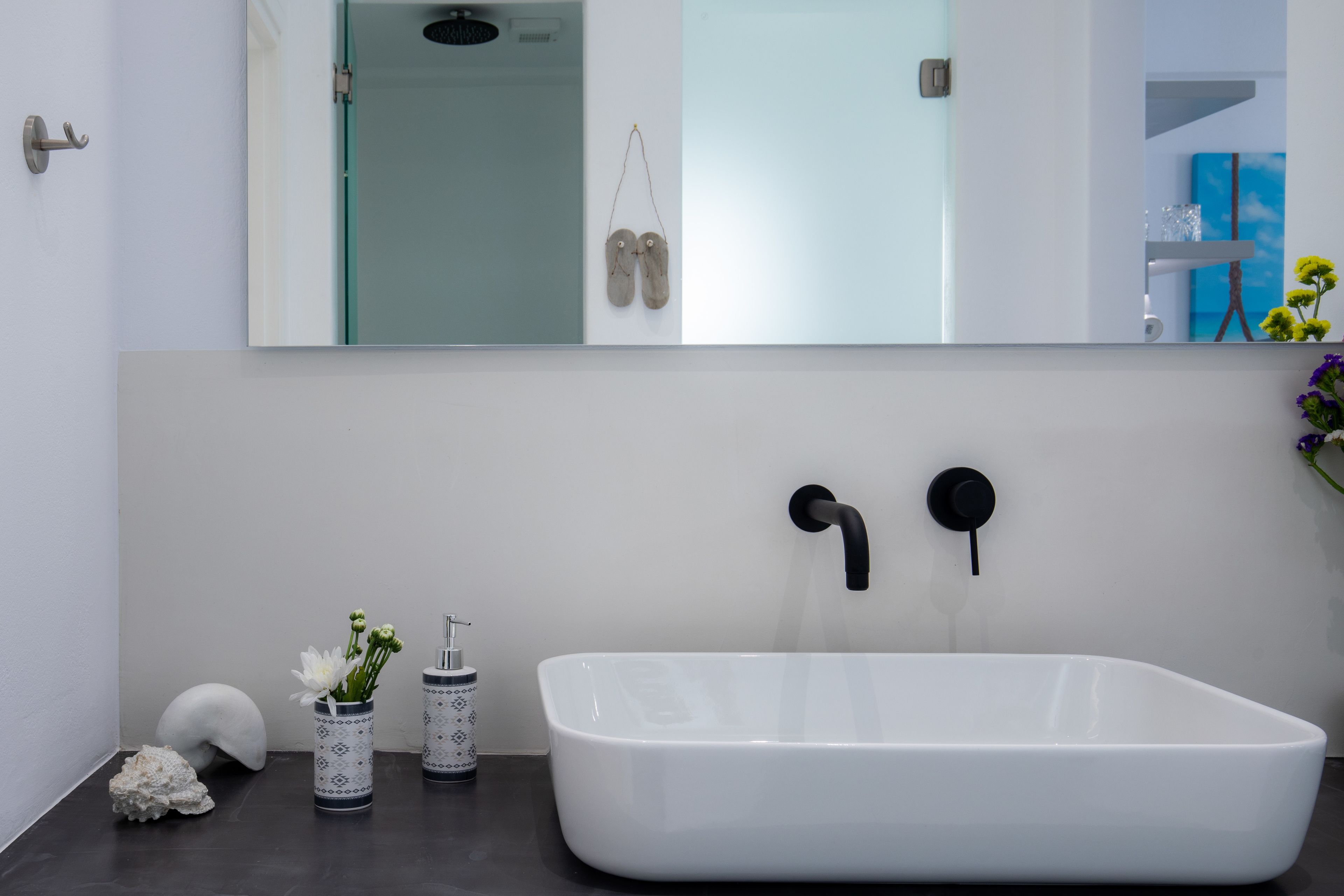 Un baño moderno con una bañera blanca grande, un espejo encima y un jarrón con flores en la encimera.