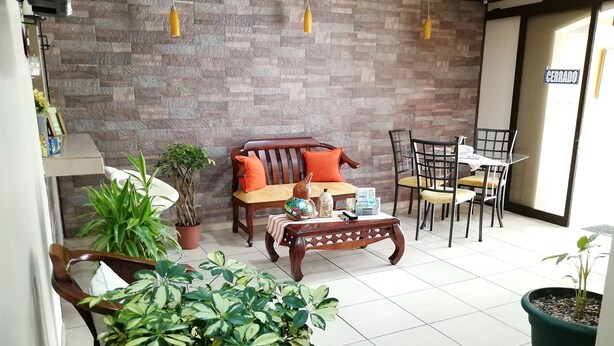 A cozy indoor seating area with a sofa, chairs, and a table, surrounded by potted plants. - Hospedaje Yaldai (Turrialba)