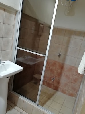 A bathroom with a glass shower enclosure, a white sink, and tiled walls.