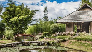 A traditional Japanese-style pavilion with a tiled roof, surrounded by a pond, rocks, and lush greenery. - Hospedaje Yaldai (Turrialba)
