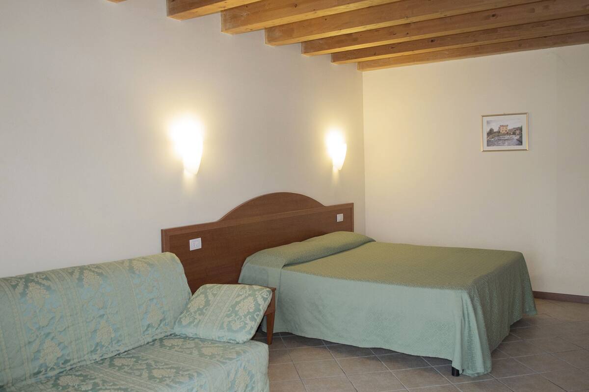 Une chambre avec deux lits simples, un canapé, des poutres apparentes en bois au plafond et deux lampes fixées au mur.
