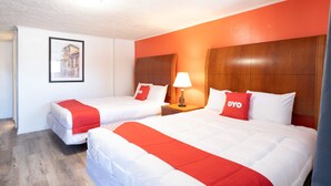 A hotel room with two beds, each with white bedding and red accents, a wooden headboard, a nightstand with a lamp, and a framed picture on the wall. - Hotel O Atlanta Airport Jonesboro/Morrow I-75 (Jonesboro)