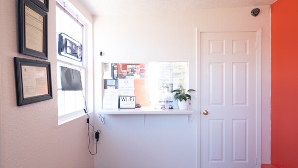 A hallway with a white door, framed certificates on the wall, a window with a 'Wi-Fi' sign, and a potted plant. - Hotel O Atlanta Airport Jonesboro/Morrow I-75 (Jonesboro)