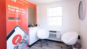 A hotel room with a large OYO app advertisement, two white chairs, a window, and a wall-mounted clock. - Hotel O Atlanta Airport Jonesboro/Morrow I-75 (Jonesboro)