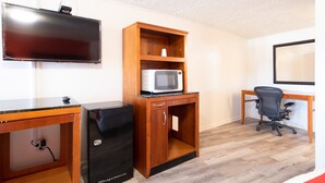 A compact room with a flat-screen TV, a microwave, a small refrigerator, a wooden desk, and a black office chair. - Hotel O Atlanta Airport Jonesboro/Morrow I-75 (Jonesboro)
