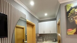 A compact kitchen with white cabinets, a microwave, and a sink. There's a wooden door and a mirror on the wall. - The Zanadu İstanbul (Istanbul)