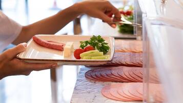A person serving food on a tray with sliced meat, cheese, and vegetables.