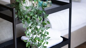 Siististi järjestetty hotellihuone, jossa on sänky, yöpöytä, jossa on hygieniatarvikkeita, ja ruukussa oleva kasvi.