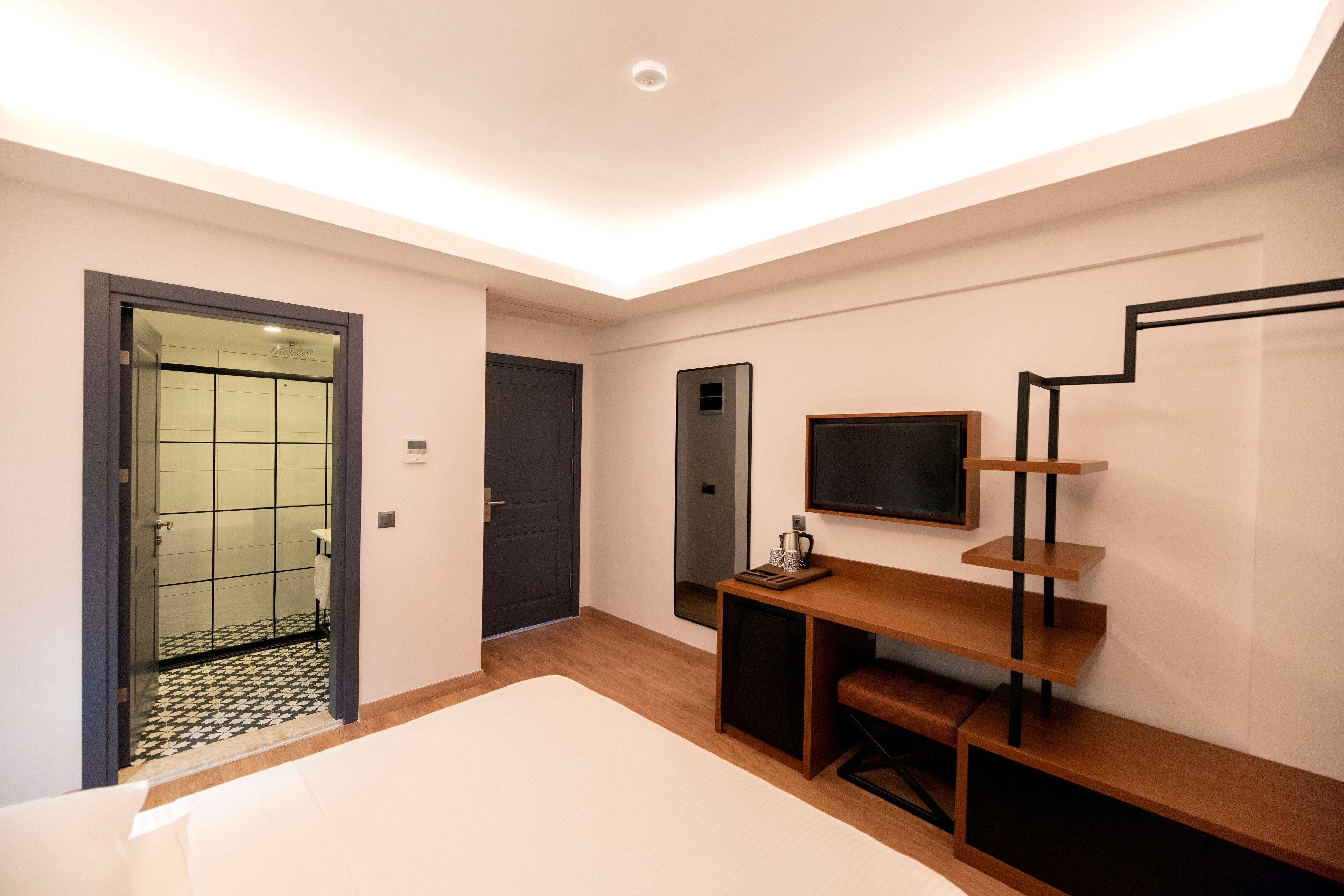 A modern bedroom with a large bed, a desk with a chair, a mirror, and a staircase.