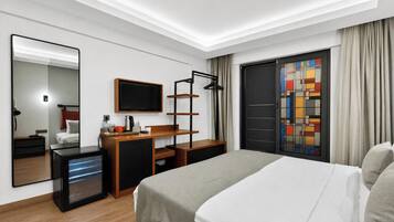 A modern hotel room with a bed, a desk with a computer, a TV, and a large window with curtains.