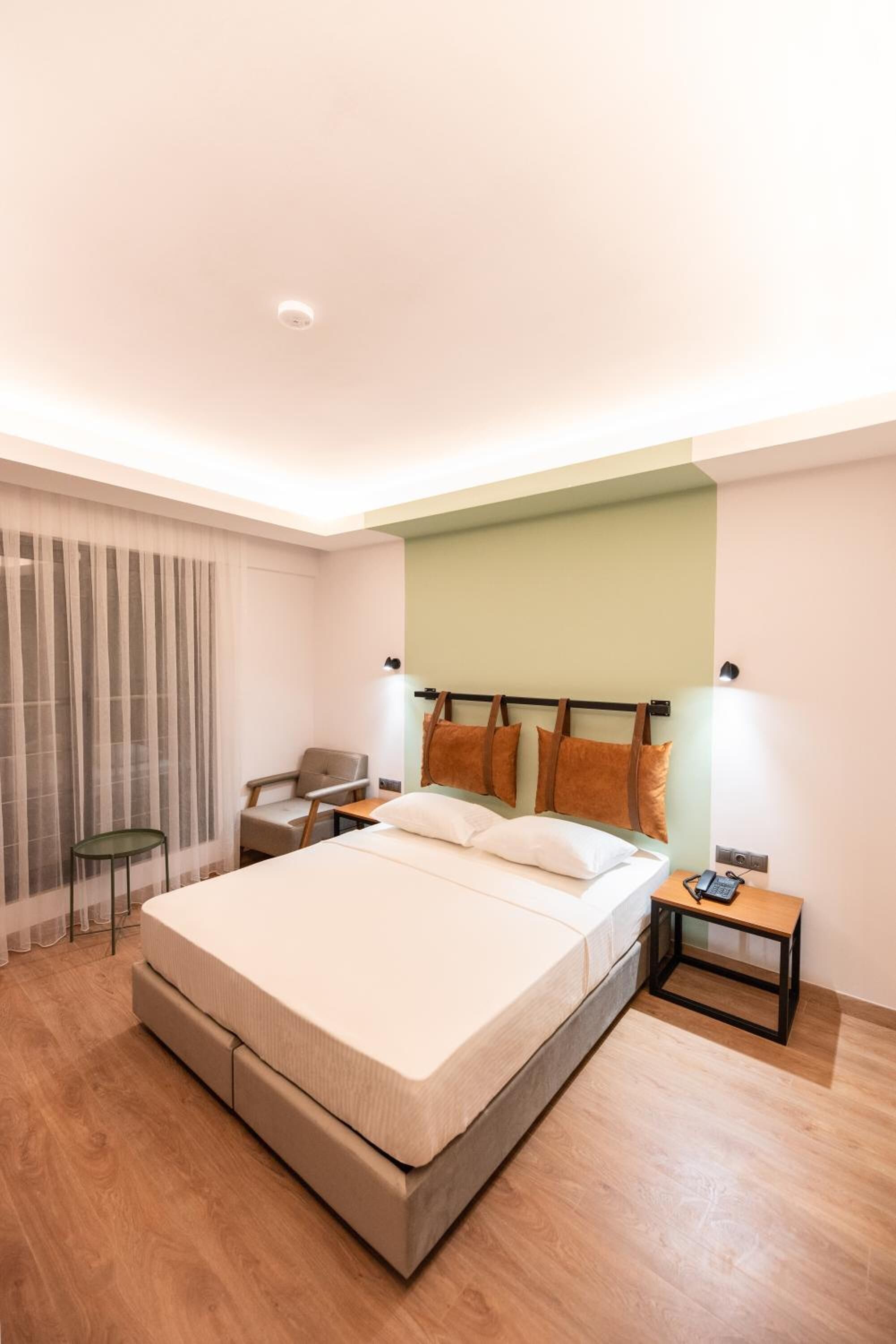 A modern hotel room with a large bed, a chair, a small table, and a nightstand.