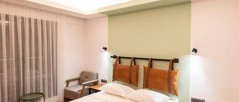 A modern hotel room with a large bed, a chair, a small table, and a nightstand.