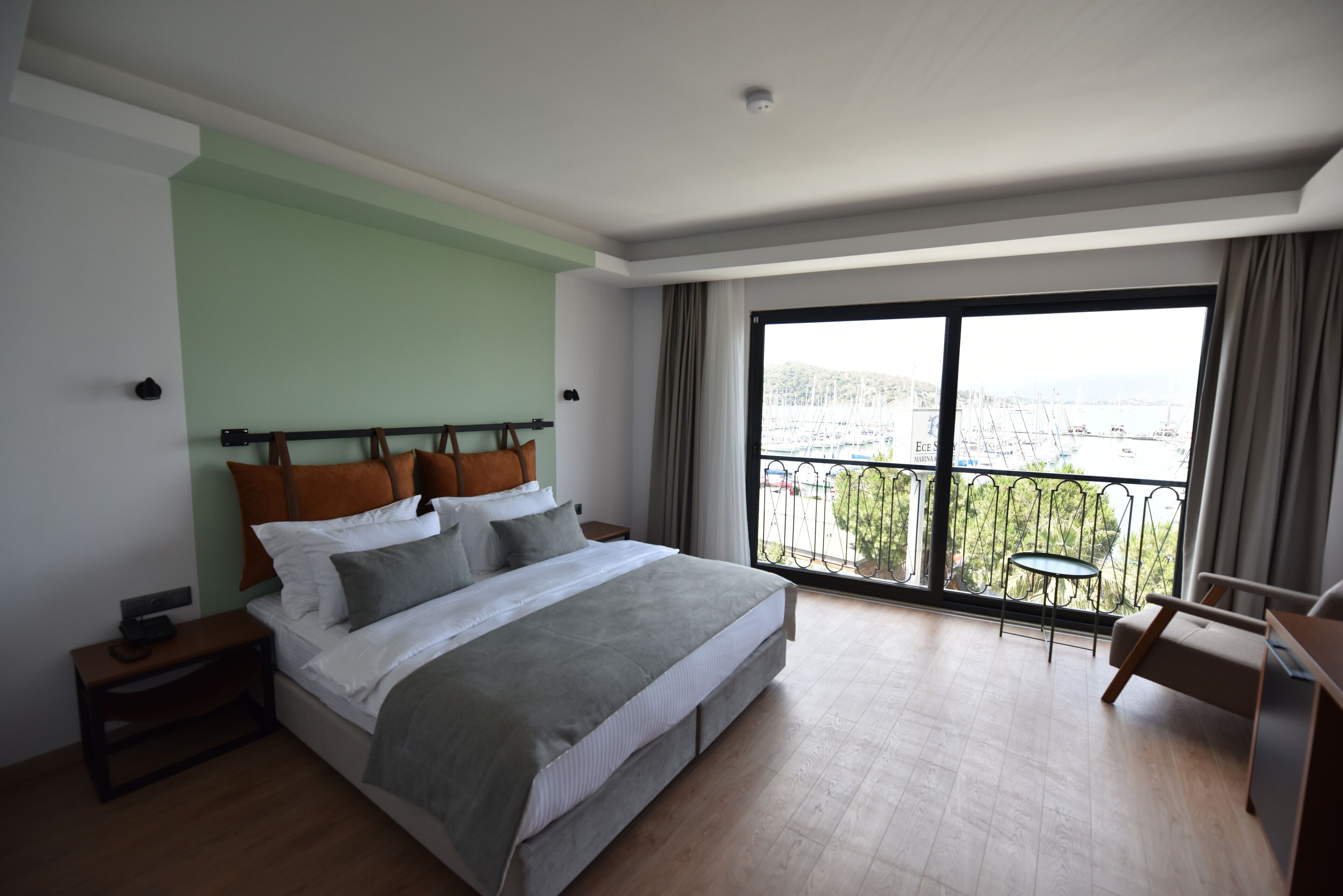 A modern bedroom with a large bed, a small table, and a balcony with a view of the city.