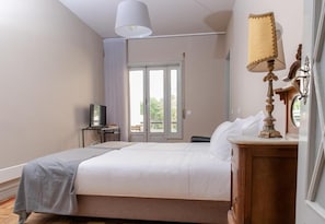 Habitación de hotel con una cama, un escritorio con lámpara, televisión y vistas al exterior a través de una puerta.