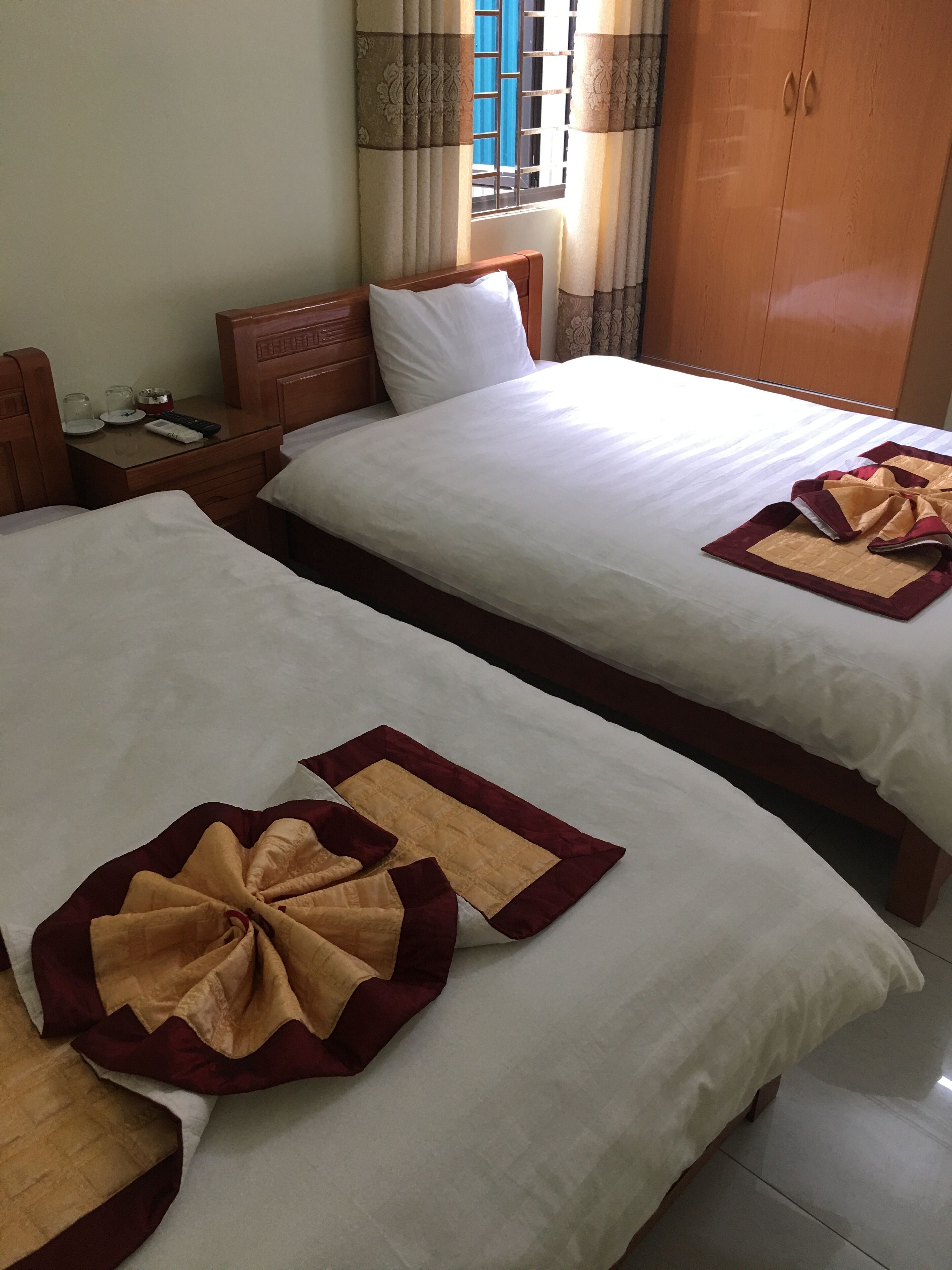 A hotel room with two beds, each with a neatly made bedspread and a decorative pillow. There is a wooden nightstand with a remote control and glasses beside one bed.