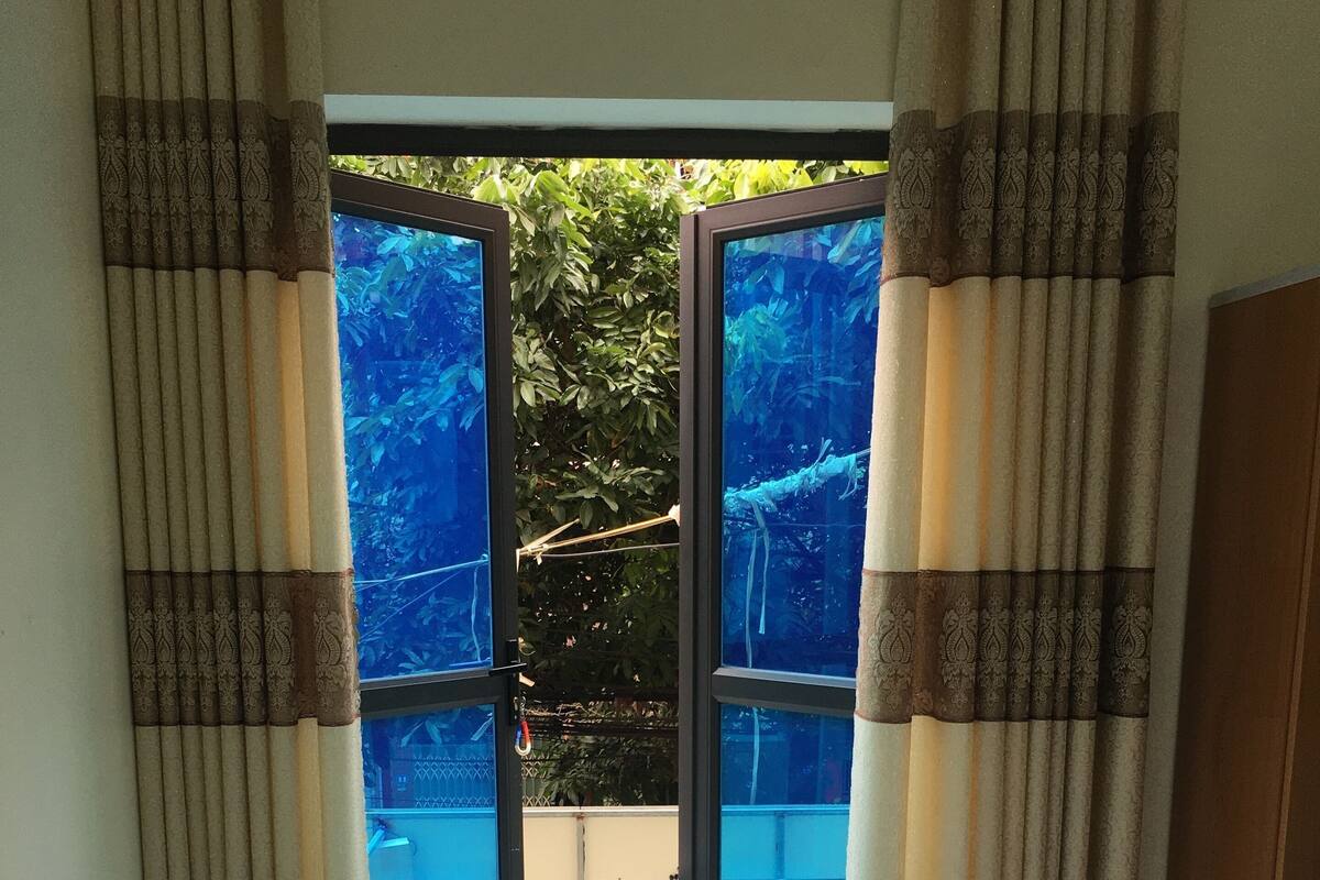 A room with a bed, curtains, and a view of an outdoor area with a water feature.