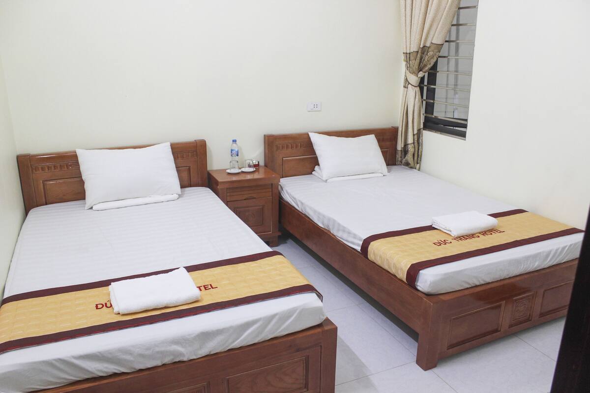 Two single beds with wooden headboards, white linens, and a yellow towel on each.